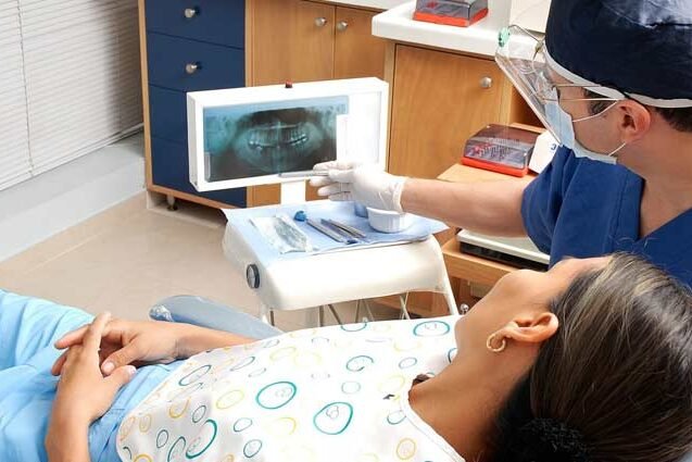 una paziente sdraiata a fianco il medico ortodontista mostra un display con una panoramica della bocca