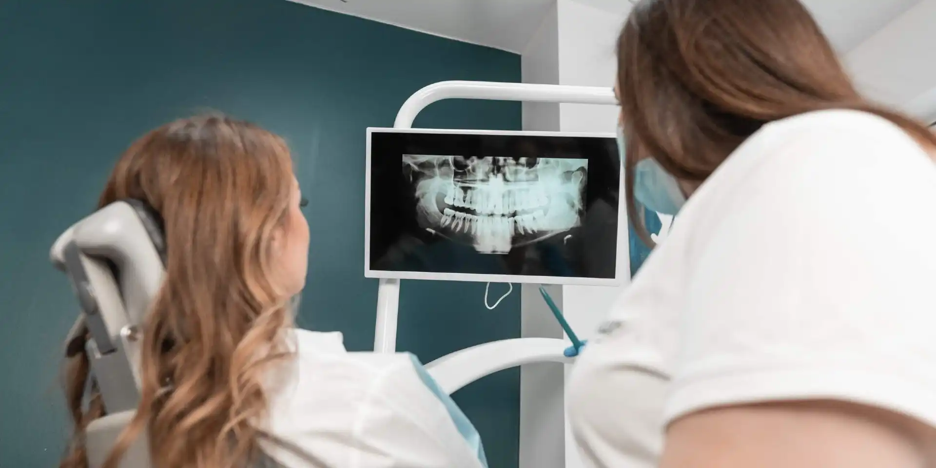 Dentista che guarda una panoramica con il paziente sul lettino