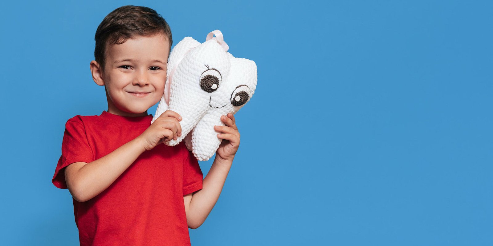 bambino sorridente su fondo azzurro, con in mano grande dente bianco di peluche
