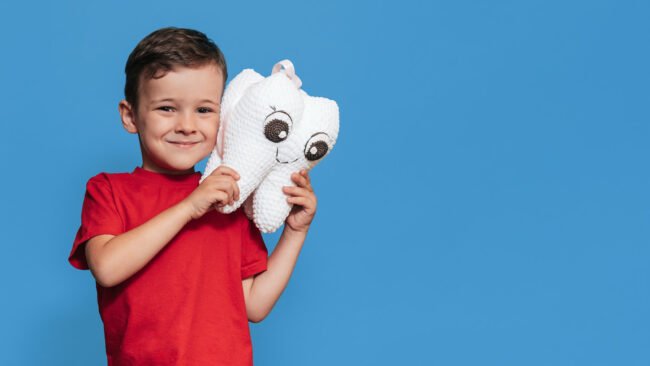 bambino sorridente su fondo azzurro, con in mano grande dente bianco di peluche