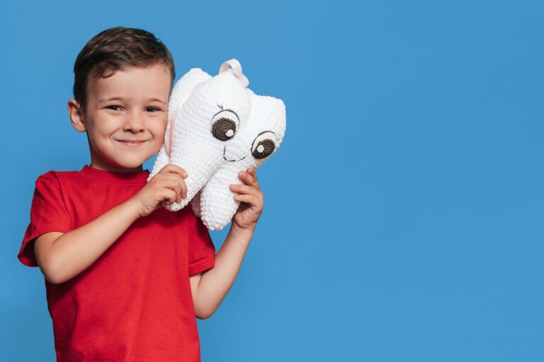 bambino sorridente su fondo azzurro, con in mano grande dente bianco di peluche